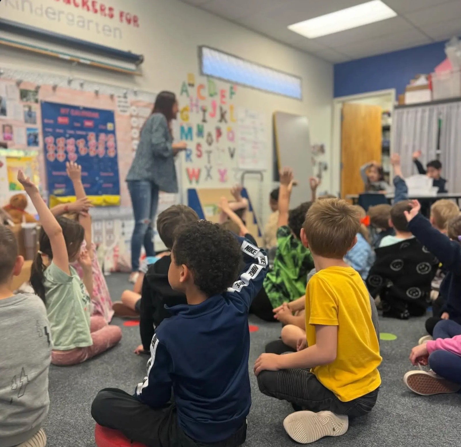 Benchmark kindergarten students raising their hands during a classroom lesson